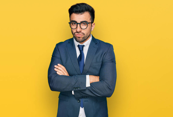 Hispanic man with beard wearing business suit and tie skeptic and nervous, disapproving expression on face with crossed arms. negative person.  - 写真・画像