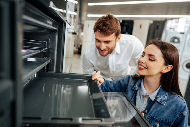 Young couple choosing new electric oven in hypermarket - Foto, Bild
