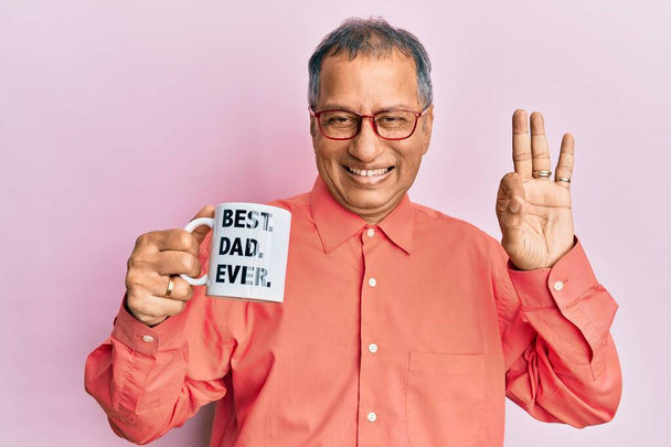 Middle age indian man drinking mug of coffee with best dad ever message doing ok sign with fingers, smiling friendly gesturing excellent symbol  - Photo, Image