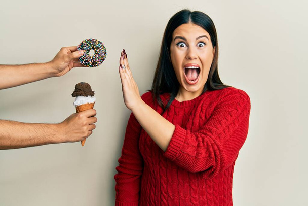 Mooie brunette vrouw zeggen nee tegen snoep op een gezond dieet vieren gek en verbaasd voor succes met open ogen schreeuwen opgewonden.  - Foto, afbeelding