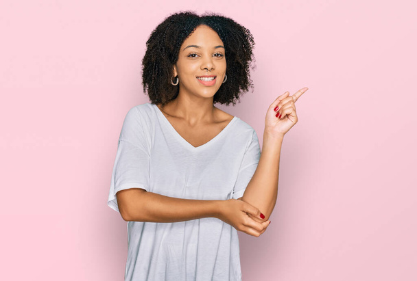 Fiatal afro-amerikai lány alkalmi ruhát visel egy nagy mosollyal az arcán, mutató kézzel és ujjal oldalra nézi a kamerát.  - Fotó, kép