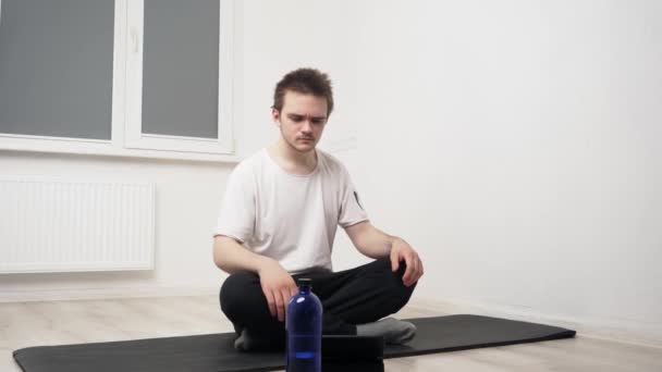 Un joven deportista realiza ejercicios sobre una alfombra negra, repitiendo lo que está sucediendo en la tableta, hace ejercicios para fortalecer el cuerpo y el espíritu. Concepto de entrenamiento en casa, yoga - Imágenes, Vídeo