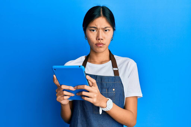 Young chinese woman wearing cook apron using touchpad skeptic and nervous, frowning upset because of problem. negative person.  - Φωτογραφία, εικόνα