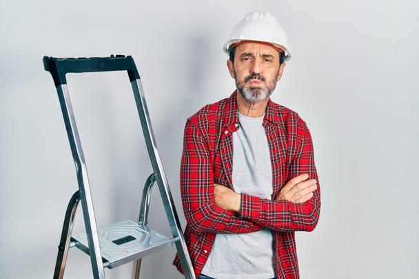 Middle age hispanic worker man with arms crossed gesture using ladder puffing cheeks with funny face. mouth inflated with air, catching air.  - Photo, Image
