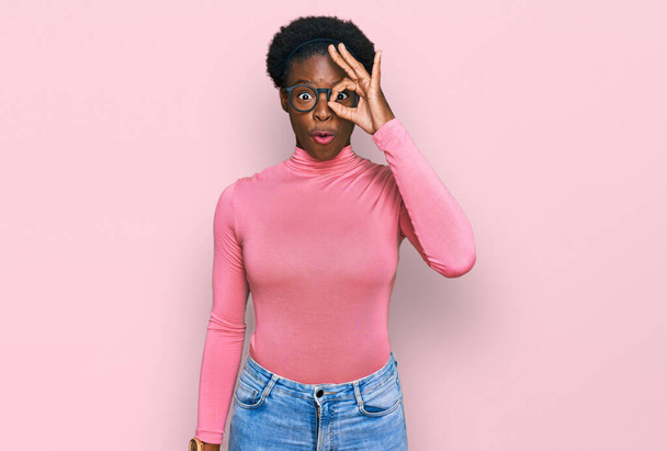 Молода афроамериканська дівчина, одягнена в повсякденний одяг і окуляри, роблять гарний жест шокований здивованим обличчям, дивлячись крізь пальці. невіруючий вираз.  - Фото, зображення