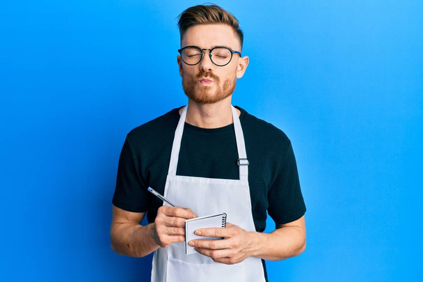 Young redhead man wearing waiter apron taking order looking at the camera blowing a kiss being lovely and sexy. love expression.  - Photo, Image