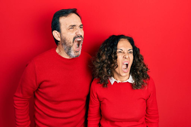 Párek hispánských žen středního věku a muž, kteří se objímají a stojí vedle sebe, vztekle a šíleně křičí, frustrovaní a zuřiví, křičí vzteky. vztek a agresivní koncept.  - Fotografie, Obrázek
