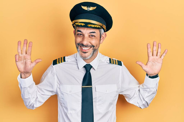 Yakışıklı, orta yaşlı, gri saçlı, uçak pilotu üniforması giyen, dokuz numaralı parmağını gösterip, gülümseyen, kendinden emin ve mutlu bir adam..  - Fotoğraf, Görsel
