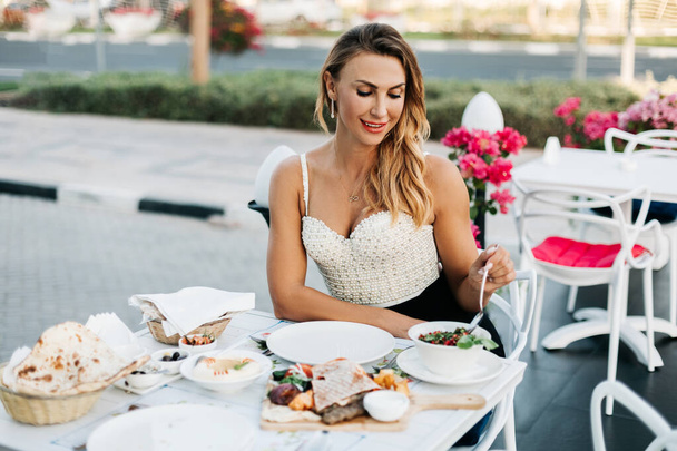 スタイリッシュな笑顔の女性が屋外カフェのテラスで昼食を取っています。健康食品、昼食休憩 - 写真・画像