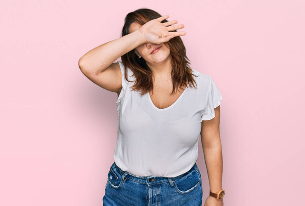 Young plus size woman wearing casual white t shirt covering eyes with arm, looking serious and sad. sightless, hiding and rejection concept  - Photo, Image