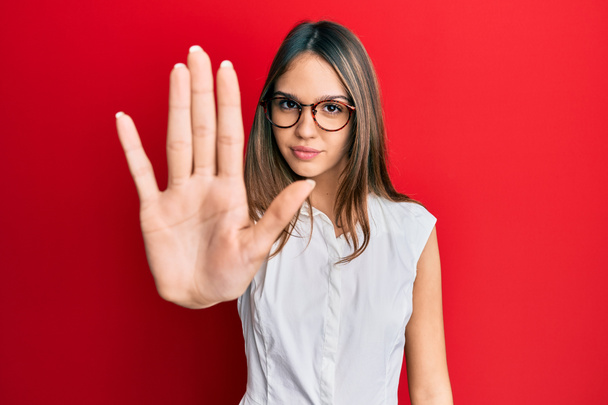 Young brunette woman wearing casual clothes and glasses doing stop sing with palm of the hand. warning expression with negative and serious gesture on the face.  - Photo, Image