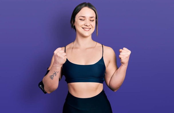 Young hispanic woman wearing sportswear excited for success with arms raised and eyes closed celebrating victory smiling. winner concept.  - Foto, Imagen