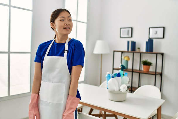 Mladá Číňanka v čistší uniformě, stojící doma a dívající se stranou s úsměvem na tváři, přirozený výraz. jistota smíchu.  - Fotografie, Obrázek