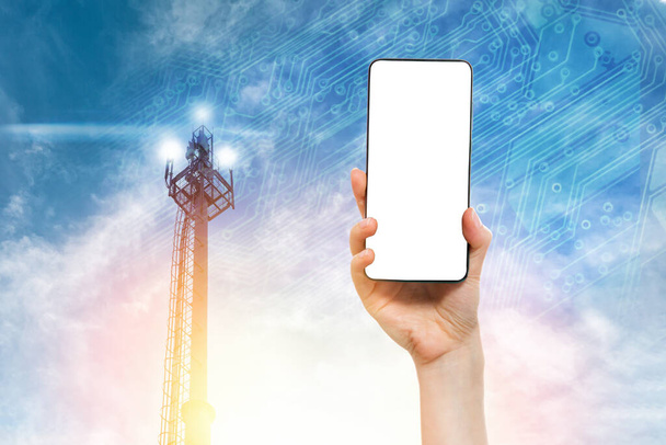 La mano di una donna tiene uno smartphone contro un cielo blu con una torre di telecomunicazioni 5G. Scherza. Concetto di tecnologia moderna e telecomunicazioni. - Foto, immagini