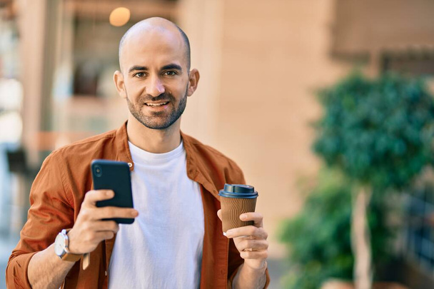 Genç Latin kökenli kel adam akıllı telefon kullanıyor. Şehirde kahve içiyor.. - Fotoğraf, Görsel