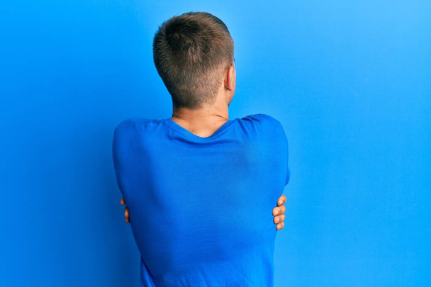 Jeune homme caucasien portant un t-shirt bleu décontracté s'embrassant heureux et positif à partir de l'arrière. amour de soi et soins de soi  - Photo, image