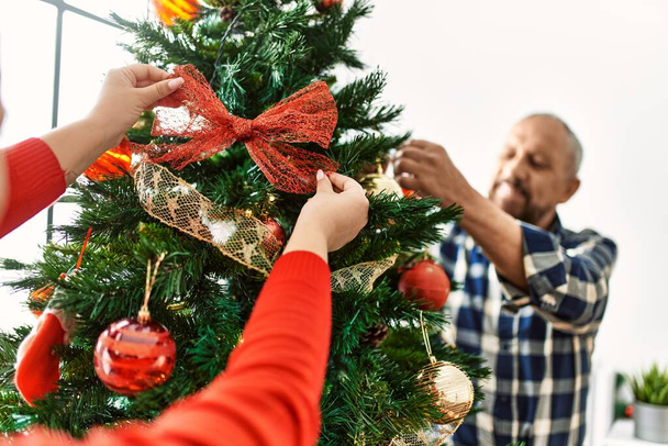 Young daughter and senior father together celebrating christmas at home, hanging christmas ornaments on the tree - Fotó, kép