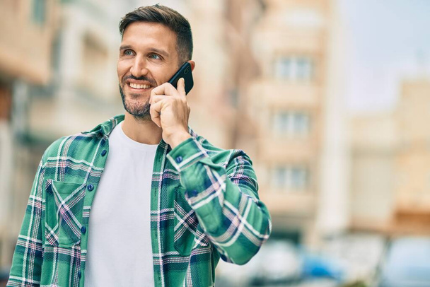 Giovane uomo caucasico sorridente felice parlando sullo smartphone in città. - Foto, immagini