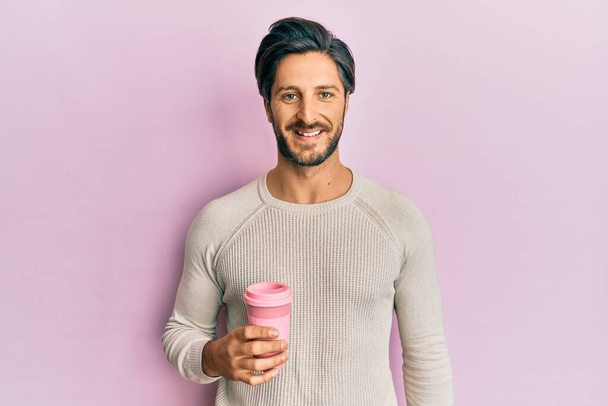 Fiatal spanyol férfi iszik egy csésze kávét elvitt pozitív és boldog álló és mosolygó magabiztos mosollyal mutatja fogak  - Fotó, kép