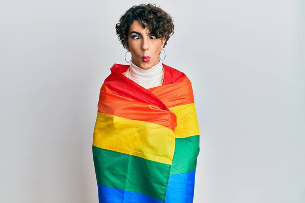 Jongeman draagt vrouw make-up verpakt in regenboog lgbtq vlag maken vis gezicht met mond en squinting ogen, gek en komisch.  - Foto, afbeelding