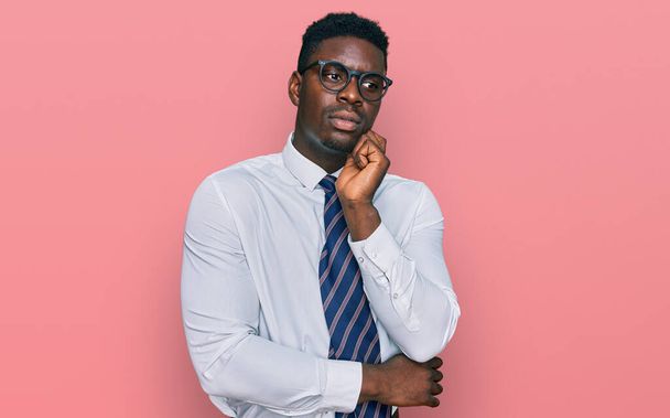 Handsome business black man wearing white shirt and tie serious face thinking about question with hand on chin, thoughtful about confusing idea  - Foto, imagen