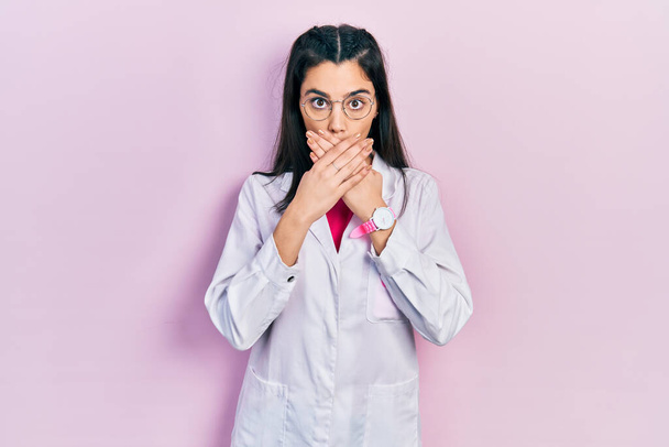 Una joven hispana con uniforme científico sorprendió cubriendo la boca con las manos por error. concepto secreto.  - Foto, imagen