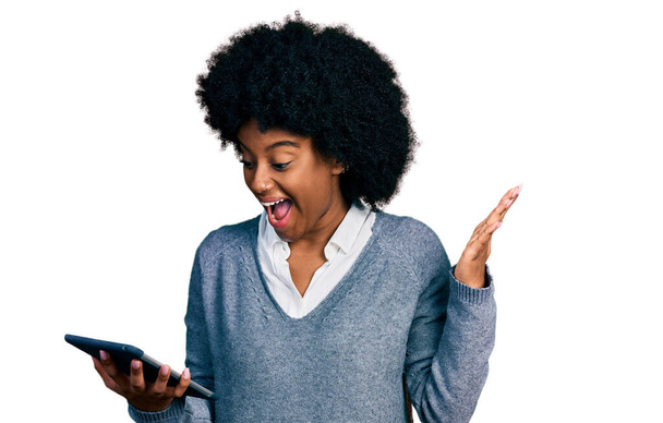 Young african american woman using touchpad device celebrating victory with happy smile and winner expression with raised hands  - Foto, Imagen