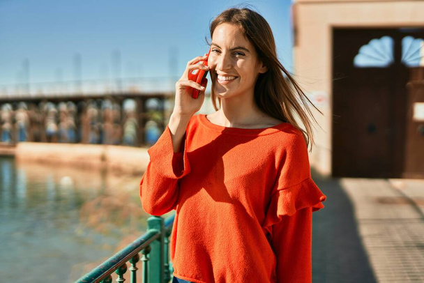 Junge hispanische Frau lächelt fröhlich auf dem Smartphone in der Stadt. - Foto, Bild