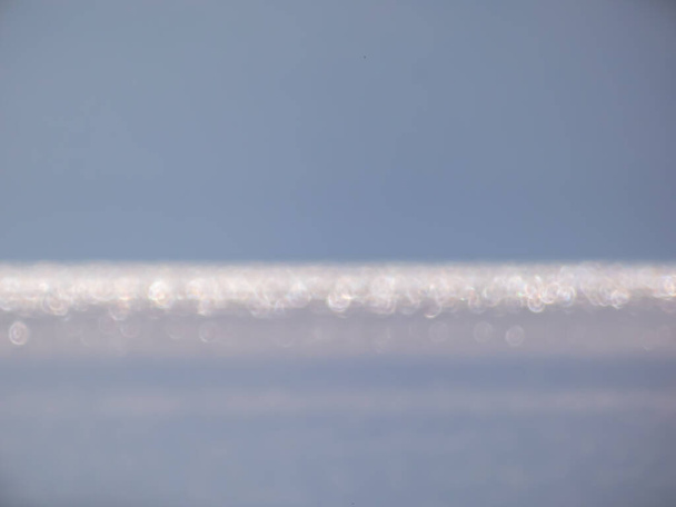 Λευκό, μπλε και γκρι εφέ bokeh και σκόπιμα θολή θέα της θάλασσας ή του ωκεανού τοπίο. Θολή και λαμπερό νερό και ουρανό φόντο με φωτογραφικό φαινόμενο bokeh - Φωτογραφία, εικόνα