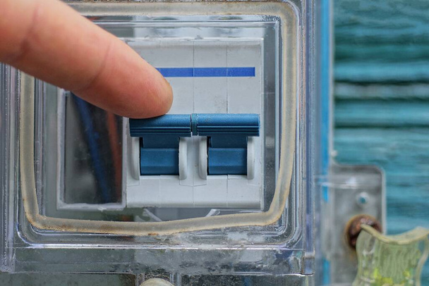 dedo en la mano apaga interruptor de palanca azul eléctrico de plástico blanco en la pared - Foto, imagen