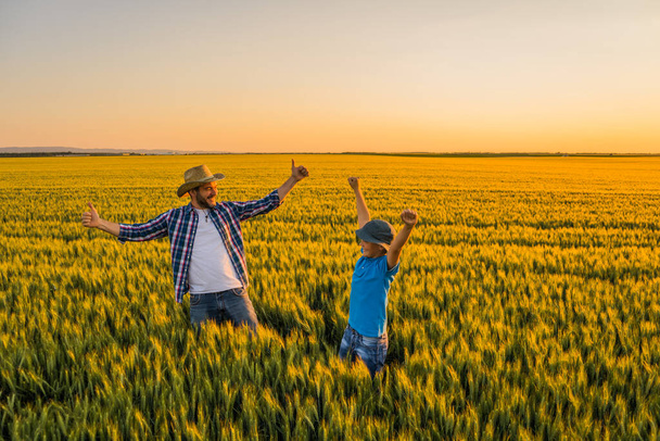Vater und Sohn stehen in ihrem wachsenden Weizenfeld. Sie freuen sich über die erfolgreiche Aussaat. - Foto, Bild