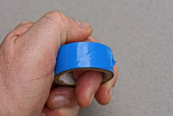 μπλε στρογγυλή πλαστική ταινία στα δάχτυλα στο χέρι σε γκρι φόντο - Φωτογραφία, εικόνα