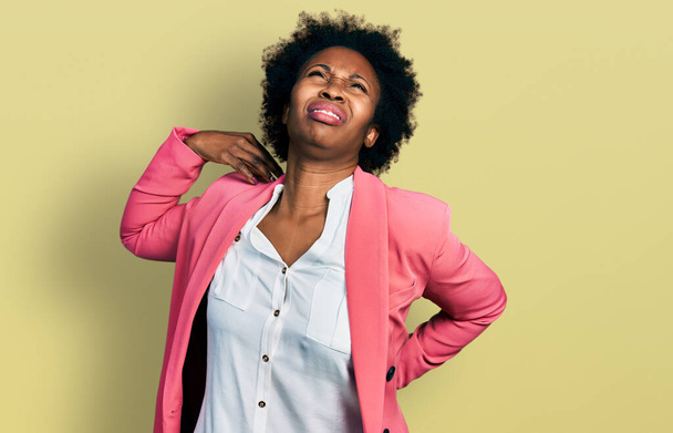 Africano mulher americana com cabelo afro vestindo jaqueta de negócios sofrendo de lesão no pescoço dor, tocando o pescoço com a mão, dor muscular  - Foto, Imagem