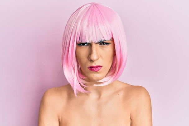 Joven hombre usando mujer maquillaje usando peluca rosa escéptico y nervioso, desaprobando la expresión en la cara con los brazos cruzados. persona negativa.  - Foto, Imagen