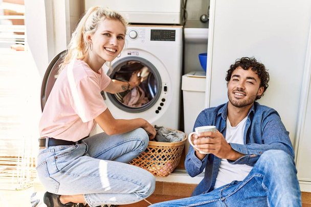 Молода пара посміхається щаслива п'є каву під час прання вдома
. - Фото, зображення