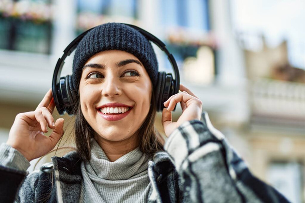 Jeune femme hispanique souriant heureux en utilisant des écouteurs à la ville. - Photo, image