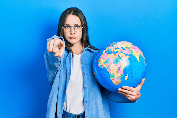 Young hispanic girl holding world ball pointing with finger to the camera and to you, confident gesture looking serious  - Foto, Imagem