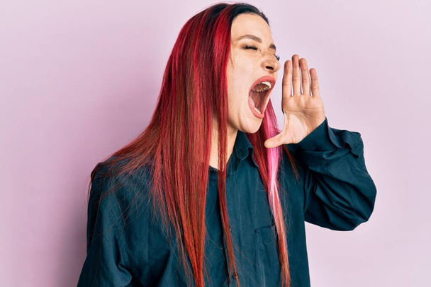 Junge kaukasische Frau in lässiger Kleidung schreit und schreit laut Seite an Seite mit der Hand auf den Mund. Kommunikationskonzept.  - Foto, Bild