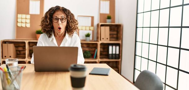 Middle age hispanic woman working at the office wearing glasses afraid and shocked with surprise expression, fear and excited face.  - Fotografie, Obrázek