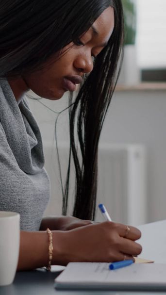 Αφροαμερικάνος φοιτητής που γράφει univeristy πληροφορίες σχετικά με σημειώσεις stickey βάζοντας στον υπολογιστή - Φωτογραφία, εικόνα