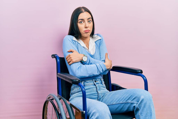 Beautiful woman with blue eyes sitting on wheelchair shaking and freezing for winter cold with sad and shock expression on face  - Фото, зображення