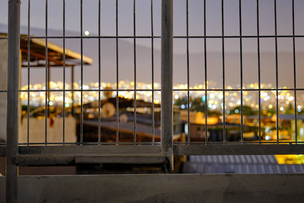 Stadsverlichting achter de metalen hekken 's nachts bij volle maan. Bursa uitzicht op de stad van laagland tot ulu berg (uludag) en vele lichten voorbij de hekken. - Foto, afbeelding