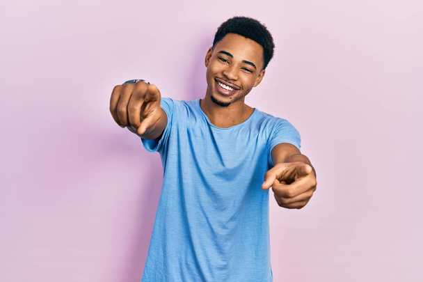 Молодой африканский американец в обычной синей футболке указывает на тебя и камеру пальцами, улыбаясь позитивно и весело  - Фото, изображение