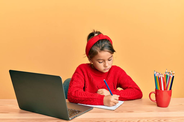 コンピュータのラップトップを使って勉強している小さな美しい女の子は、顔に深刻な表情でリラックスしました。カメラを見ているだけで.  - 写真・画像