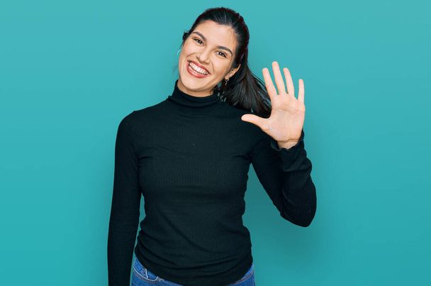Mujer hispana joven usando ropa casual mostrando y señalando hacia arriba con los dedos número cinco mientras sonríe confiado y feliz.  - Foto, Imagen