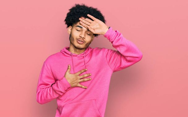 Young african american man with afro hair wearing casual pink sweatshirt touching forehead for illness and fever, flu and cold, virus sick  - Фото, зображення