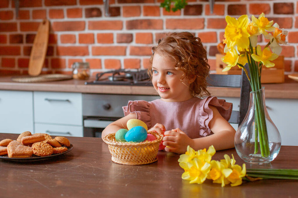 little cute girl with a basket of Easter eggs in the kitchen at home - Zdjęcie, obraz
