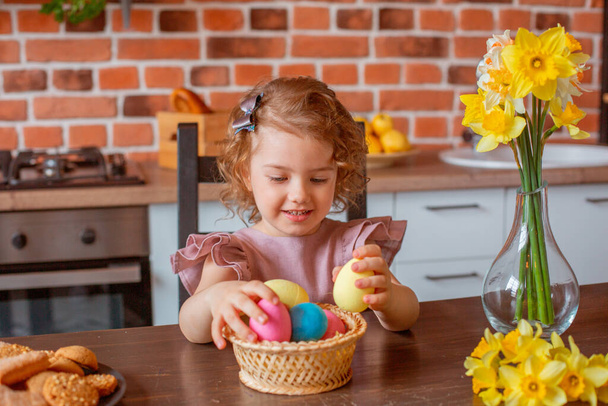 μικρό χαριτωμένο κορίτσι με ένα καλάθι πασχαλινά αυγά στην κουζίνα στο σπίτι - Φωτογραφία, εικόνα