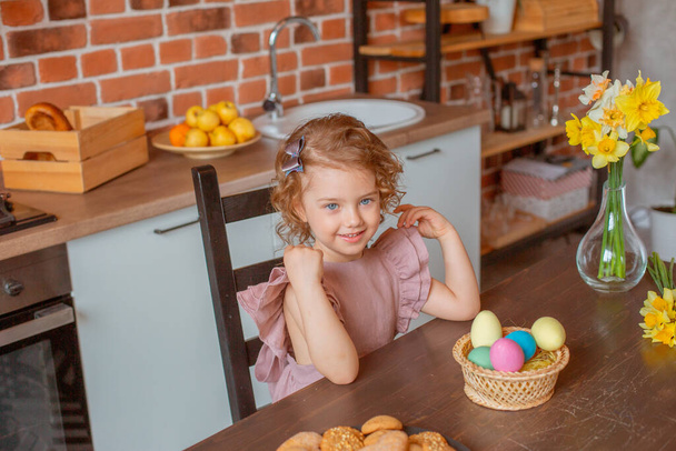 klein schattig meisje met een mand van paaseieren in de keuken thuis - Foto, afbeelding