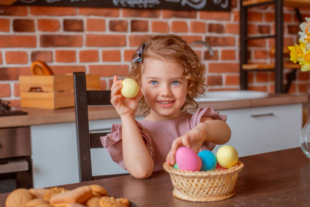 malá roztomilá dívka s košíkem velikonočních vajec v kuchyni doma - Fotografie, Obrázek